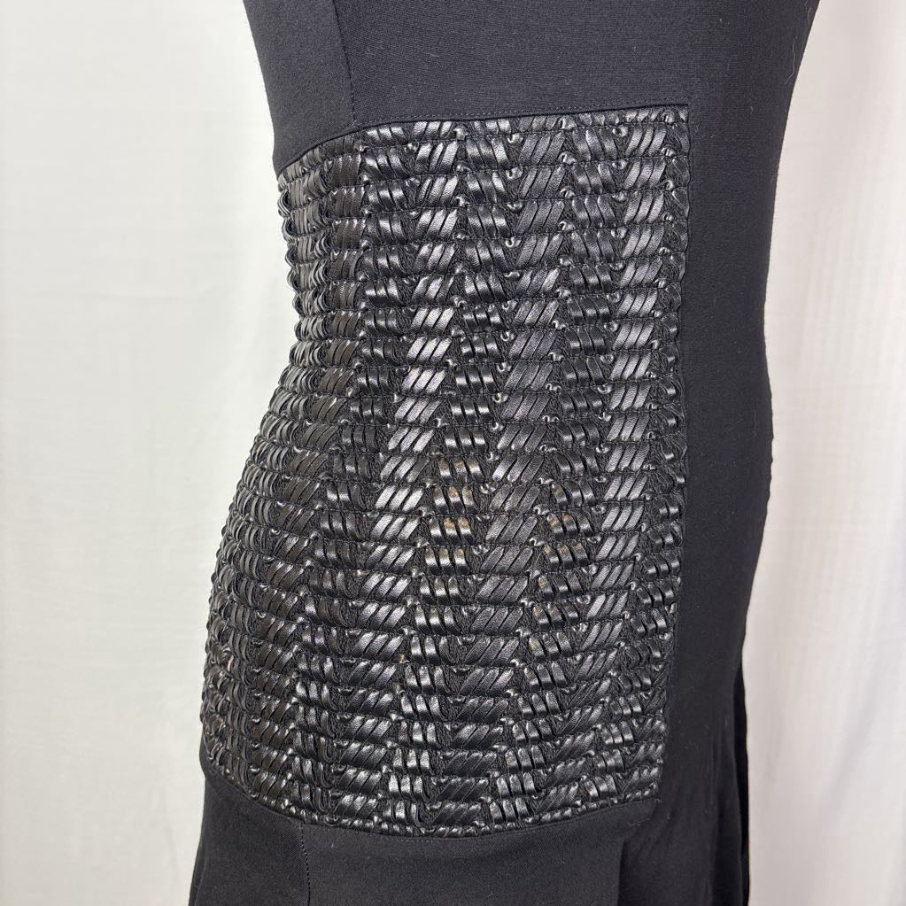 Close-up of a black dress or garment on a mannequin, showing a wide textured panel with tightly woven or braided horizontal detailing across the front.