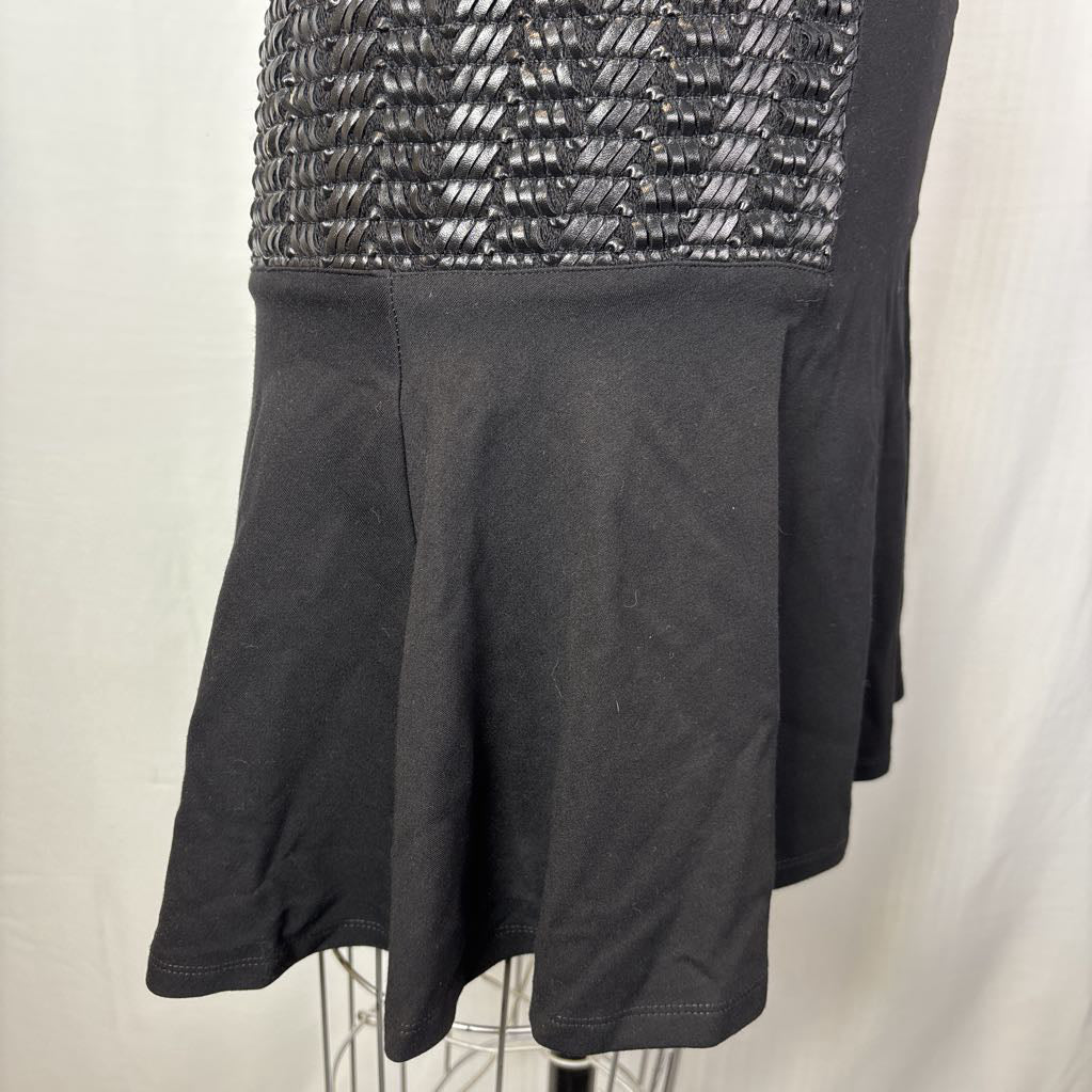 A close-up of a black dress or skirt featuring a textured, woven metallic silver upper panel and a flared black fabric lower section, displayed on a mannequin against a white background.