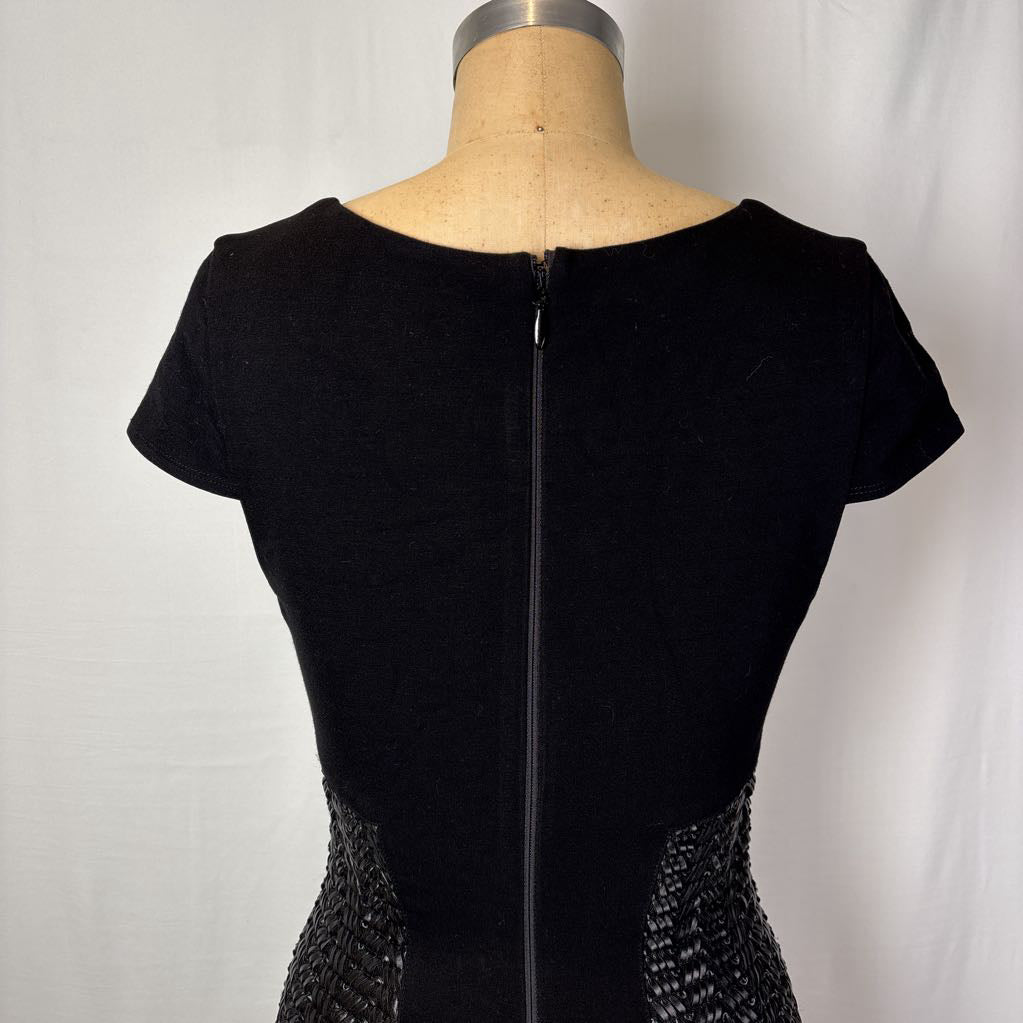 Black short-sleeve dress shown from the back on a dress form mannequin, featuring a center zipper and textured beaded side panels, against a white fabric backdrop.