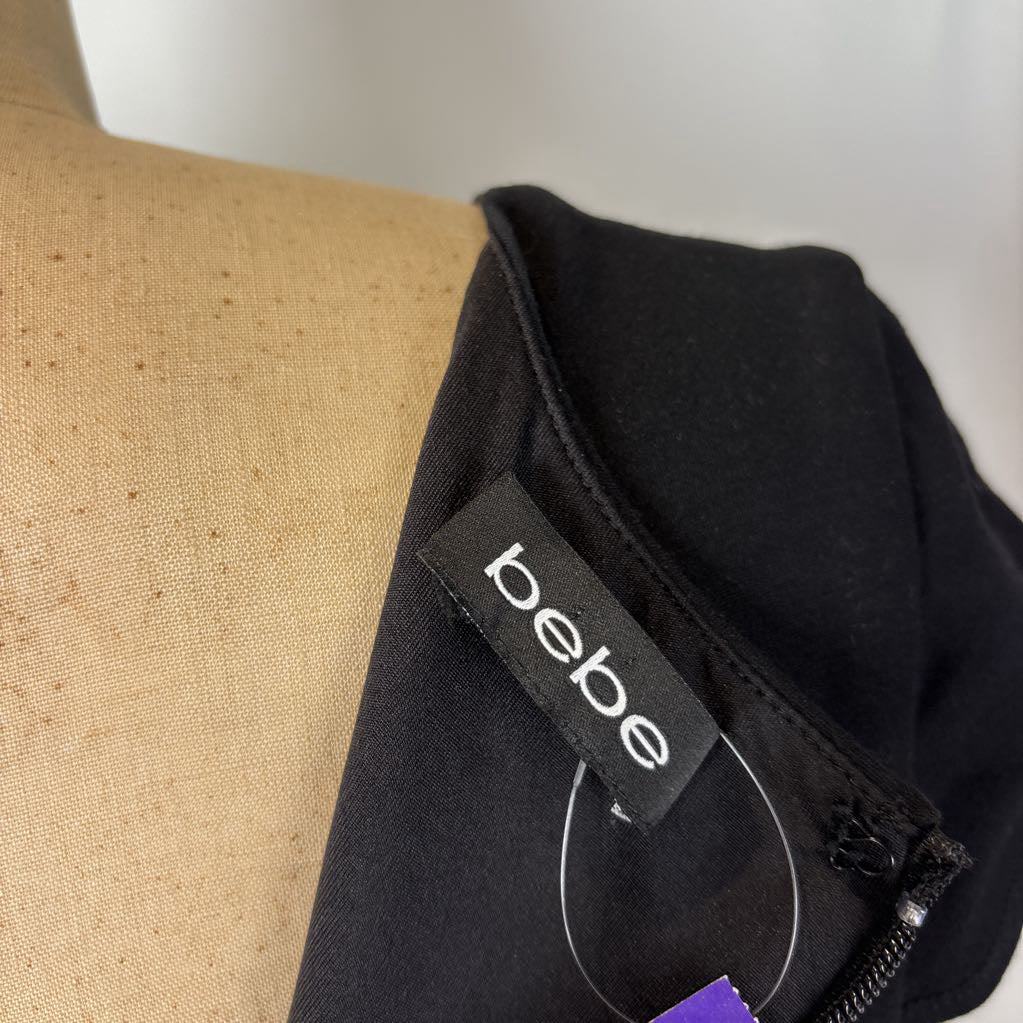 Close-up of a black garment on a tan dress form, showing a sewn-in black fabric label that reads 'bebe' in white text.