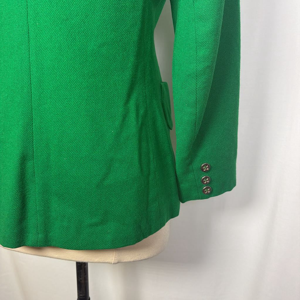 A bright green textured blazer jacket displayed on a cream-colored dress form mannequin against a white fabric backdrop. The sleeve features three decorative metallic buttons.