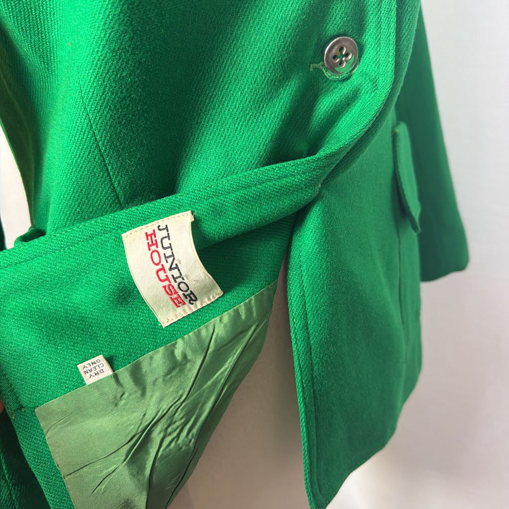 Close-up of a bright green jacket or coat with a visible sewn-in label reading 'JACKIE JONES' and a small size tag, photographed against a plain light background.