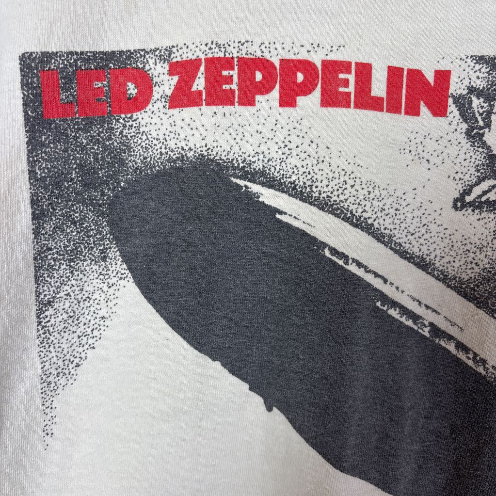 A white vintage style short sleeve t-shirt with an image of a Led Zeppelin album cover and the band's name in red letters. The shirt hangs on a wooden rack against a white background. 