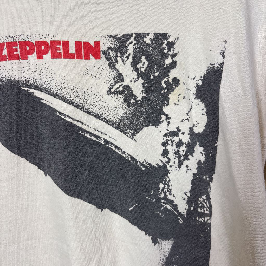 A white vintage style short sleeve t-shirt with an image of a Led Zeppelin album cover and the band's name in red letters. The shirt hangs on a wooden rack against a white background. 