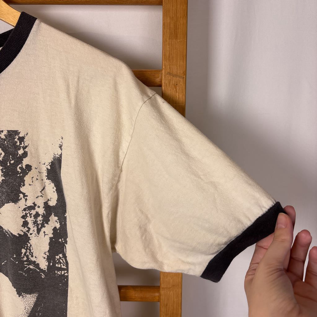 A white vintage style short sleeve t-shirt with an image of a Led Zeppelin album cover and the band's name in red letters. The shirt hangs on a wooden rack against a white background. 