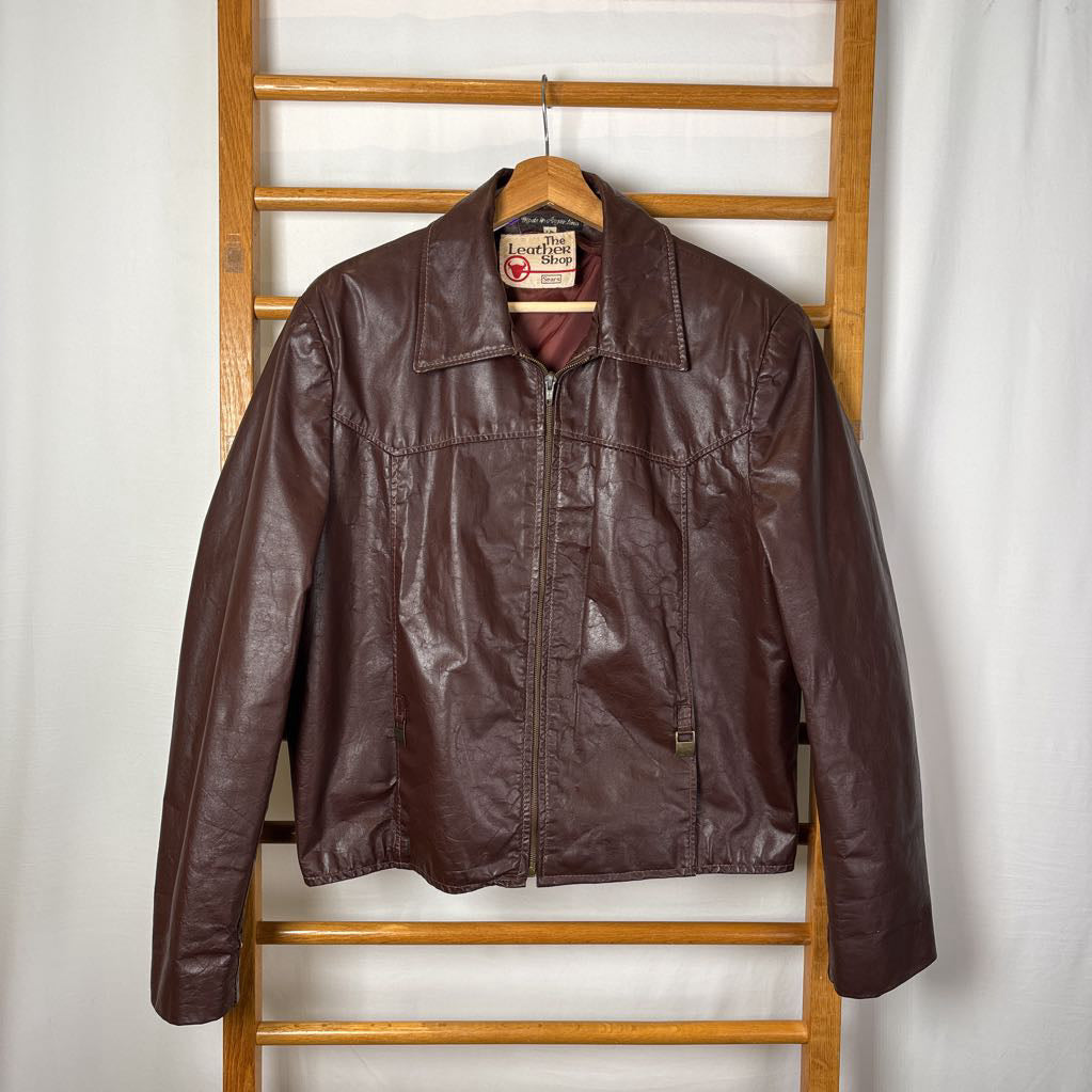 A brown leather jacket hanging on a wooden rack against a white wall.