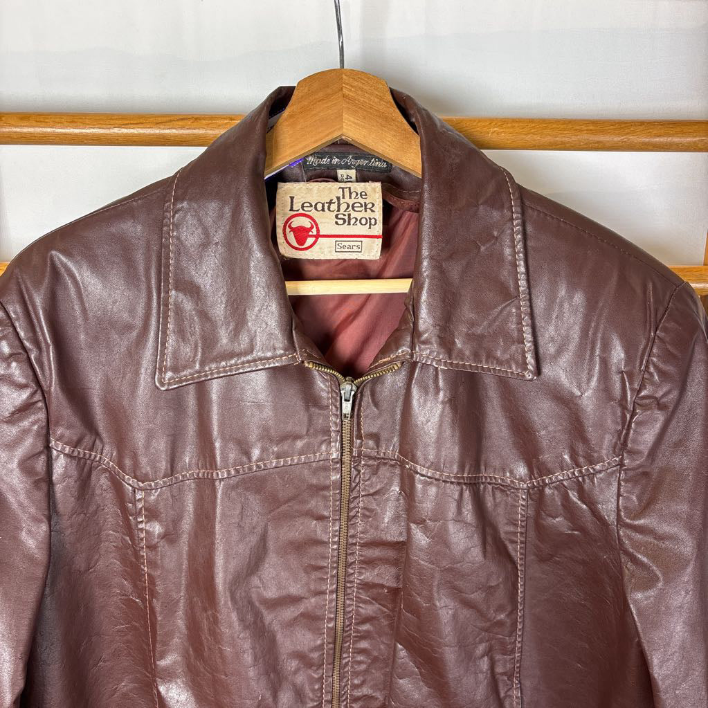 A brown leather jacket hanging on a wooden rack against a white wall.