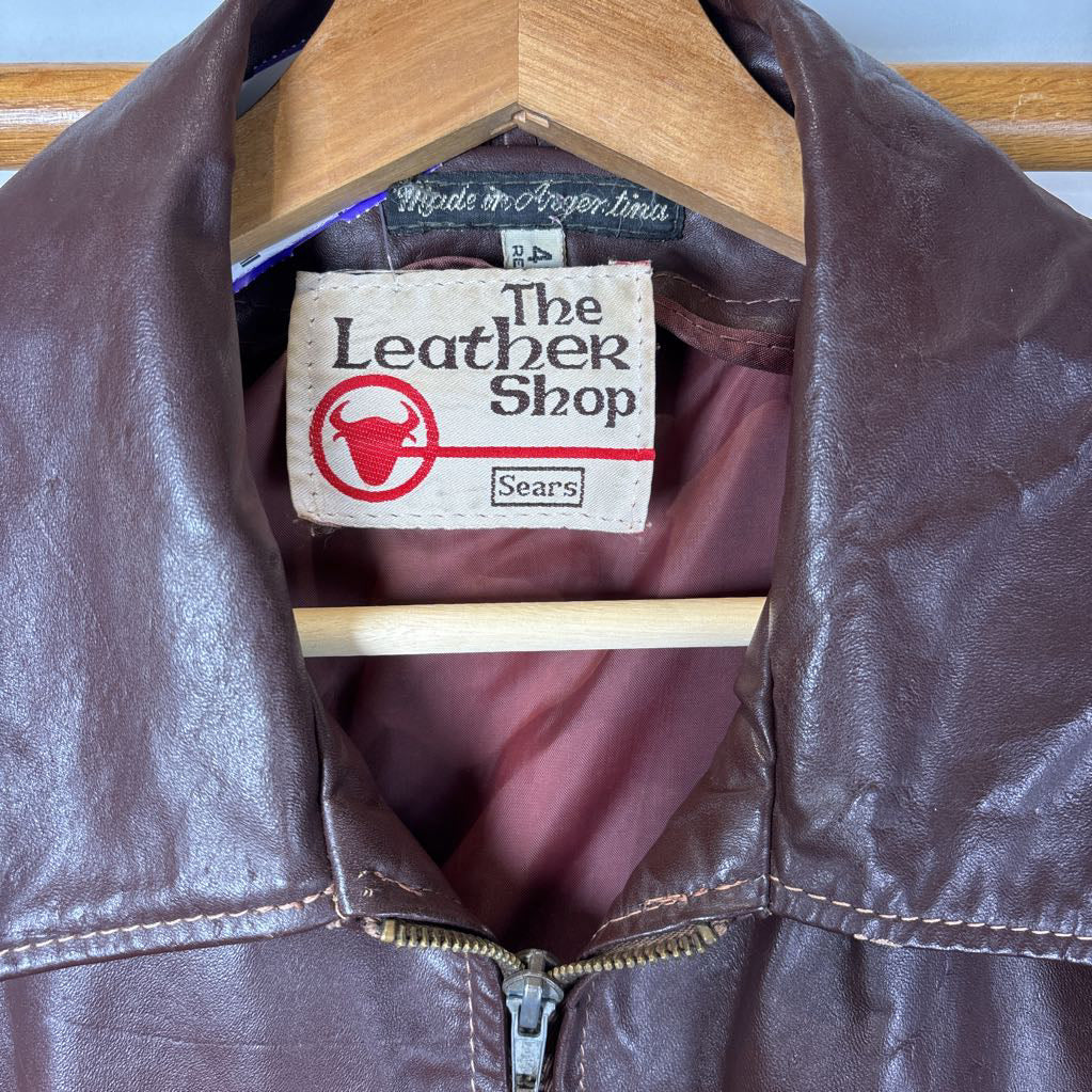 A brown leather jacket hanging on a wooden rack against a white wall.