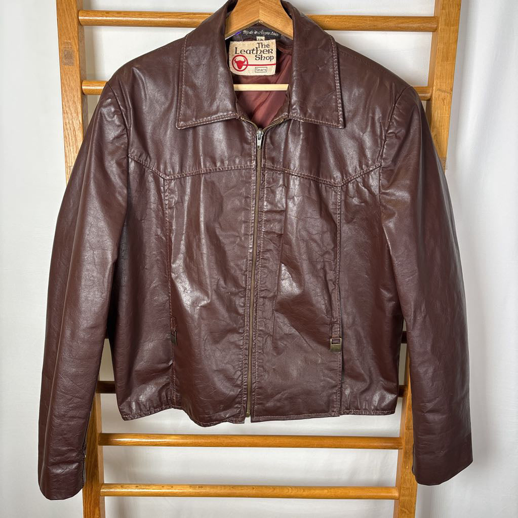 A brown leather jacket hanging on a wooden rack against a white wall.