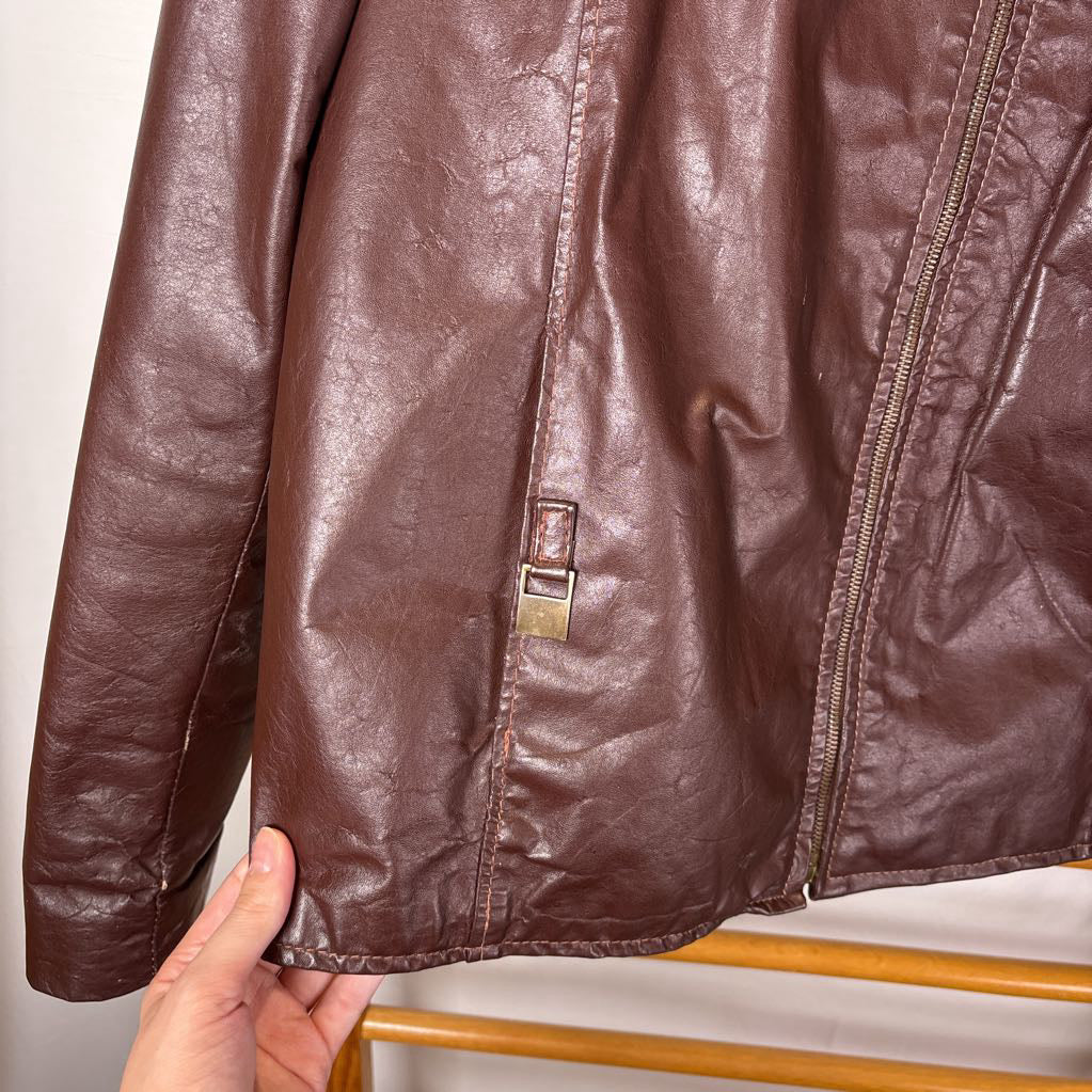 A brown leather jacket hanging on a wooden rack against a white wall.