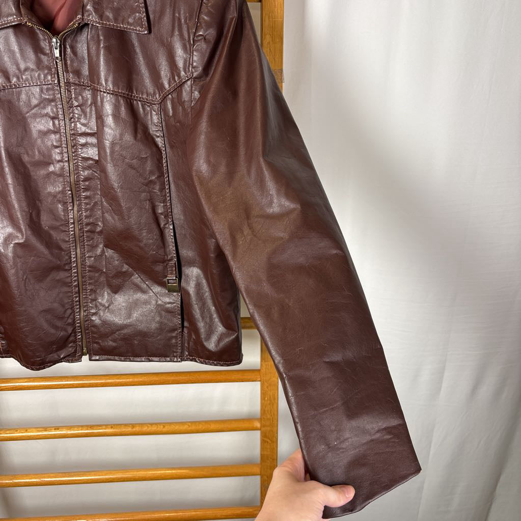 A brown leather jacket hanging on a wooden rack against a white wall.