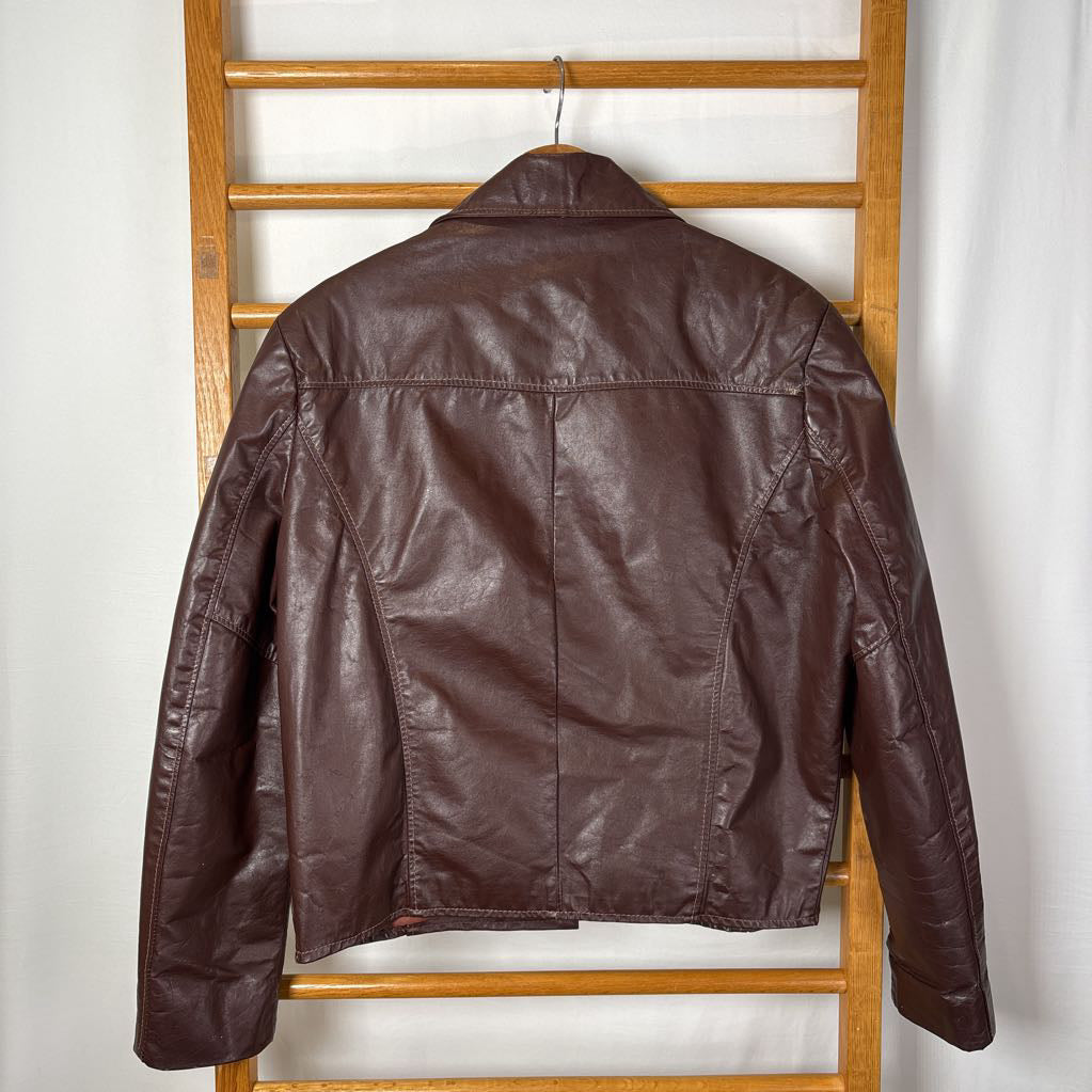 A brown leather jacket hanging on a wooden rack against a white wall.
