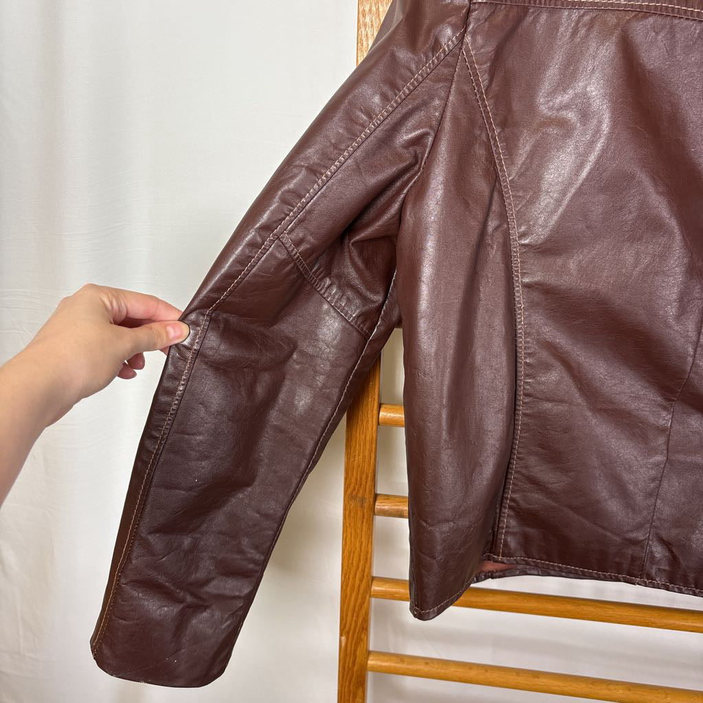 A brown leather jacket hanging on a wooden rack against a white wall.