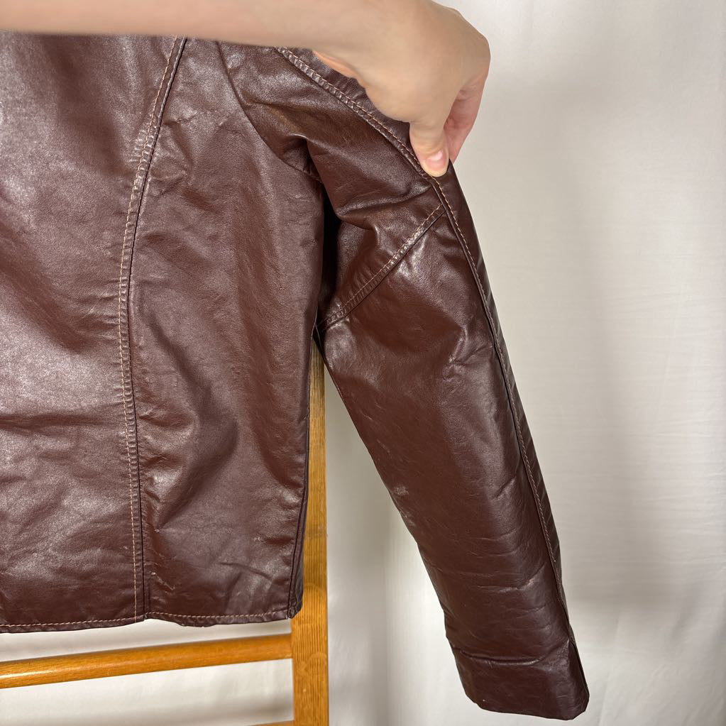 A brown leather jacket hanging on a wooden rack against a white wall.