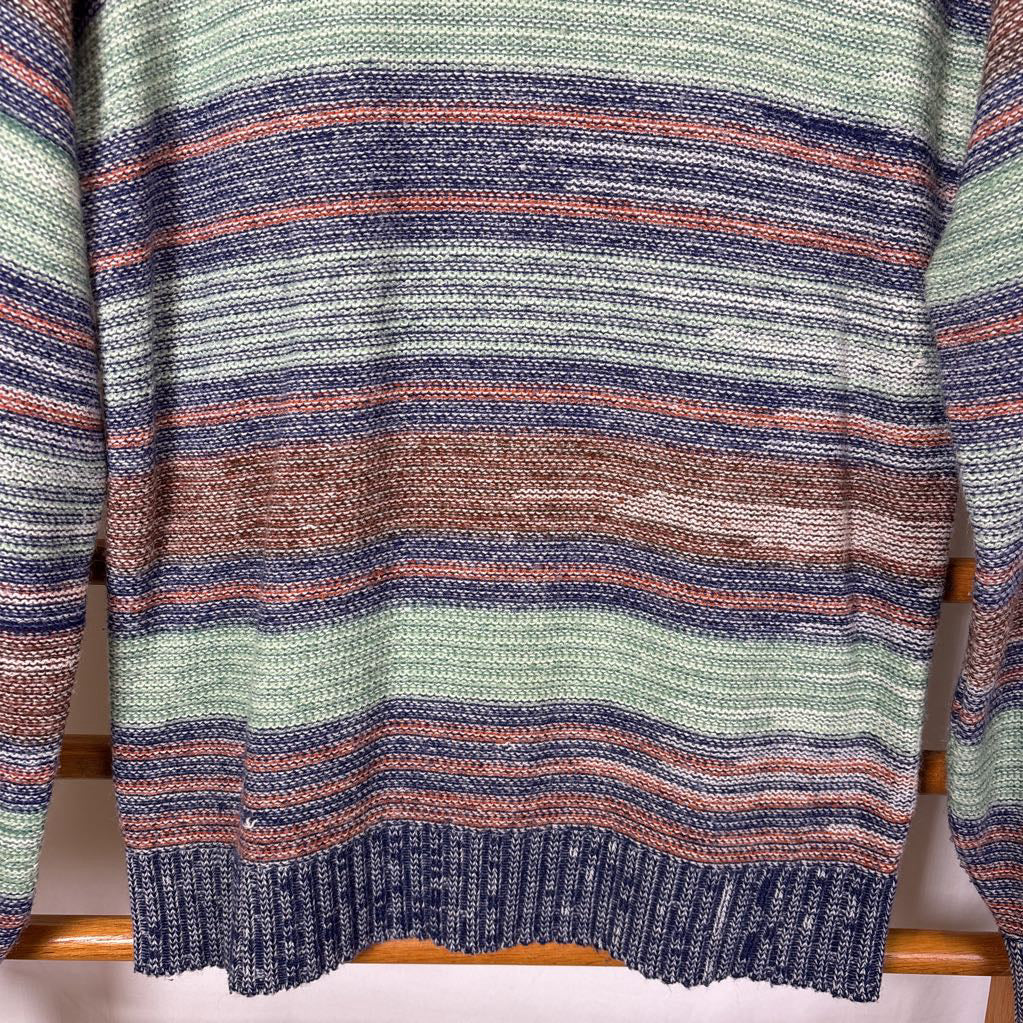 A blue, green, and brown striped knitted long sleeve sweater hanging on a wooden rack against a white background.