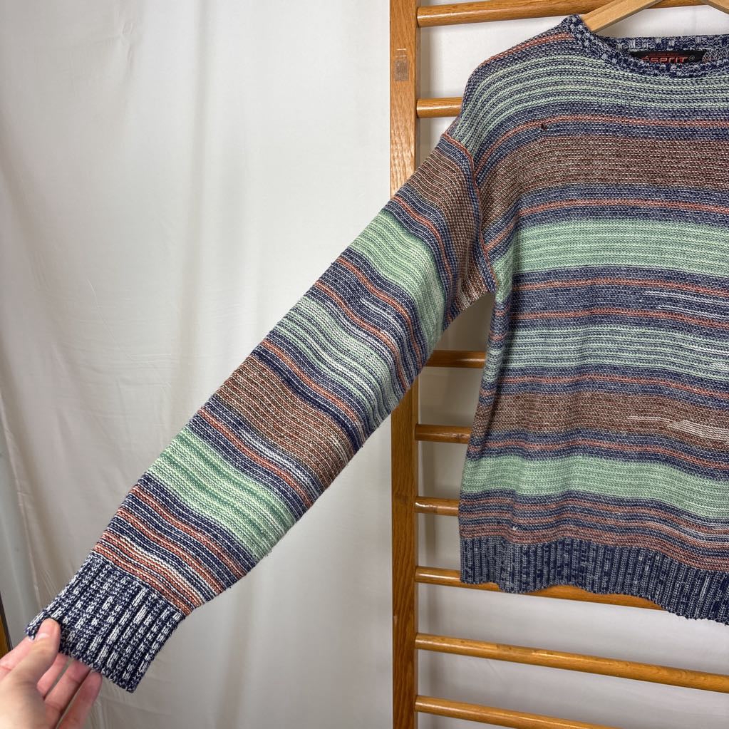A blue, green, and brown striped knitted long sleeve sweater hanging on a wooden rack against a white background.