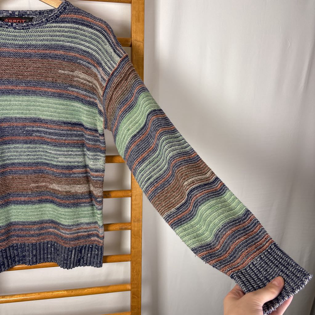 A blue, green, and brown striped knitted long sleeve sweater hanging on a wooden rack against a white background.