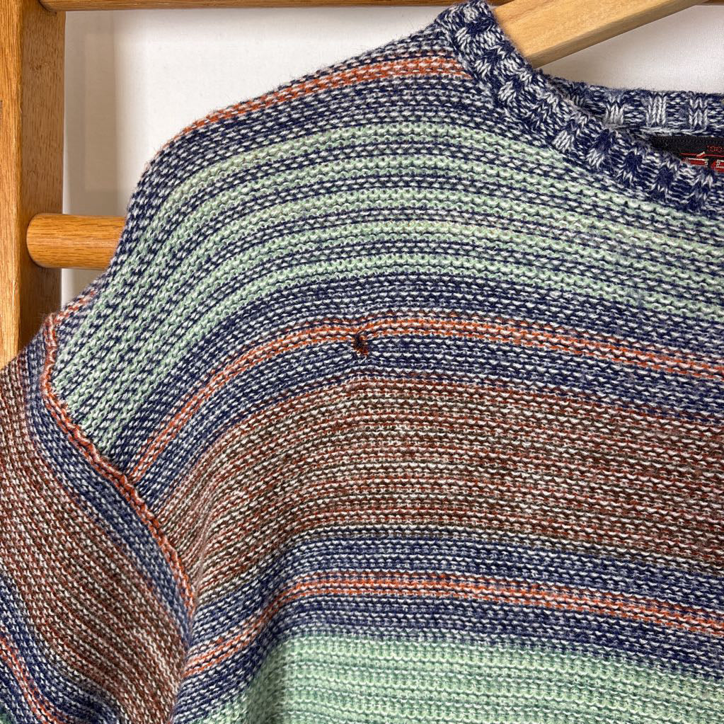 A blue, green, and brown striped knitted long sleeve sweater hanging on a wooden rack against a white background.