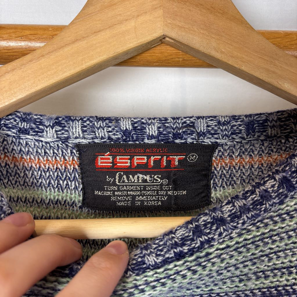 A blue, green, and brown striped knitted long sleeve sweater hanging on a wooden rack against a white background.
