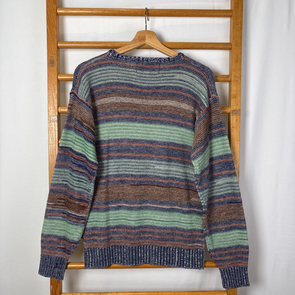 A blue, green, and brown striped knitted long sleeve sweater hanging on a wooden rack against a white background.