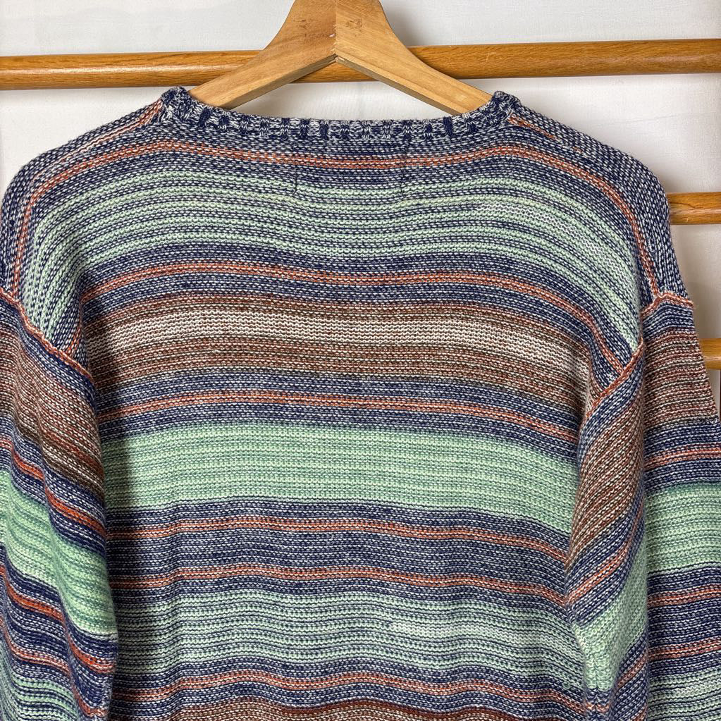 A blue, green, and brown striped knitted long sleeve sweater hanging on a wooden rack against a white background.