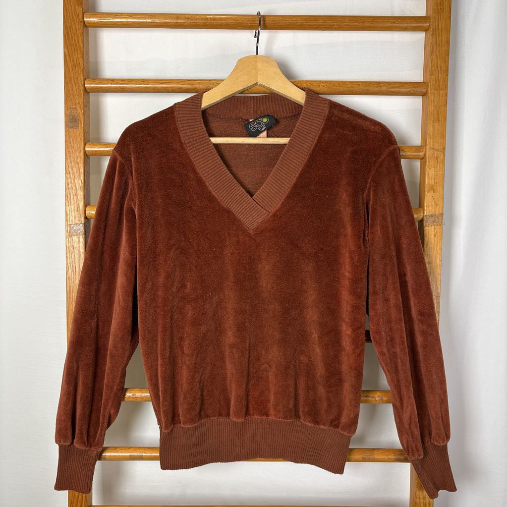 A burnt orange velour long sleeve V-neck sweater hanging on a wooden rack against a white wall.