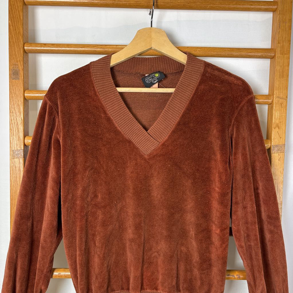 A burnt orange velour long sleeve V-neck sweater hanging on a wooden rack against a white wall.