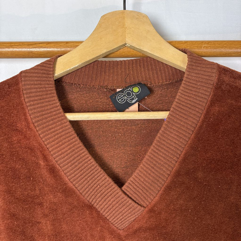 A burnt orange velour long sleeve V-neck sweater hanging on a wooden rack against a white wall.