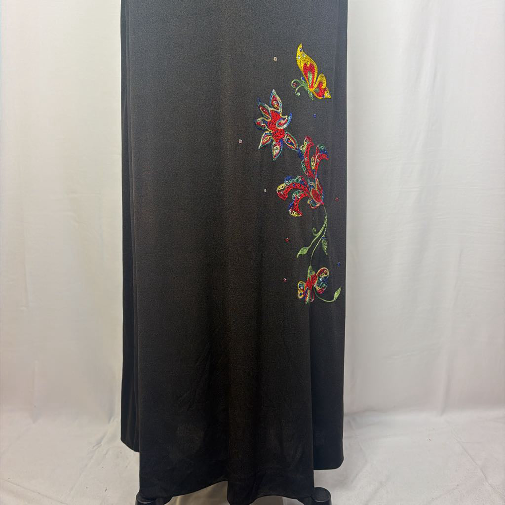 A black maxi dress with a butterfly and floral embroidery at the bottom. This dress is on a mannequin in front of a white wall. 