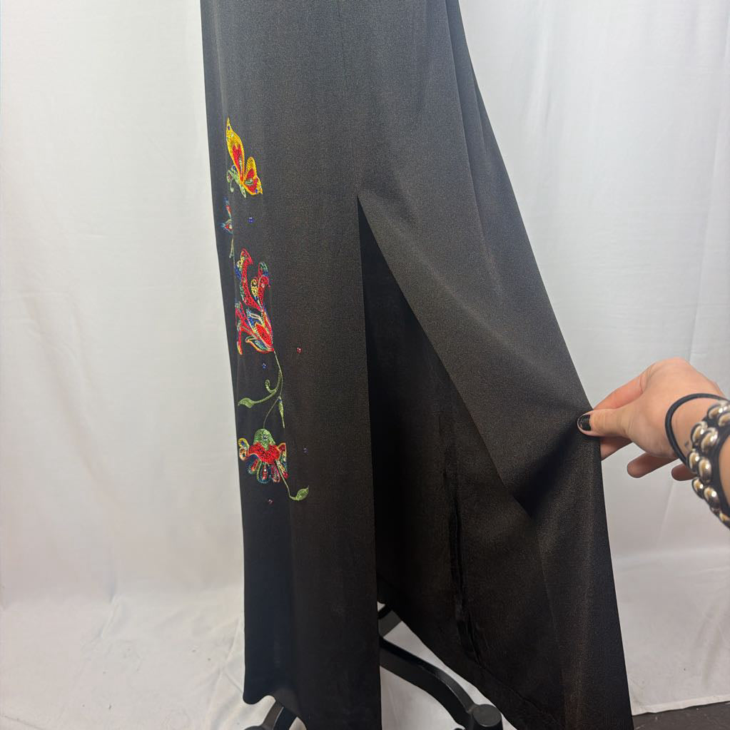 A black maxi dress with a butterfly and floral embroidery at the bottom. This dress is on a mannequin in front of a white wall. 
