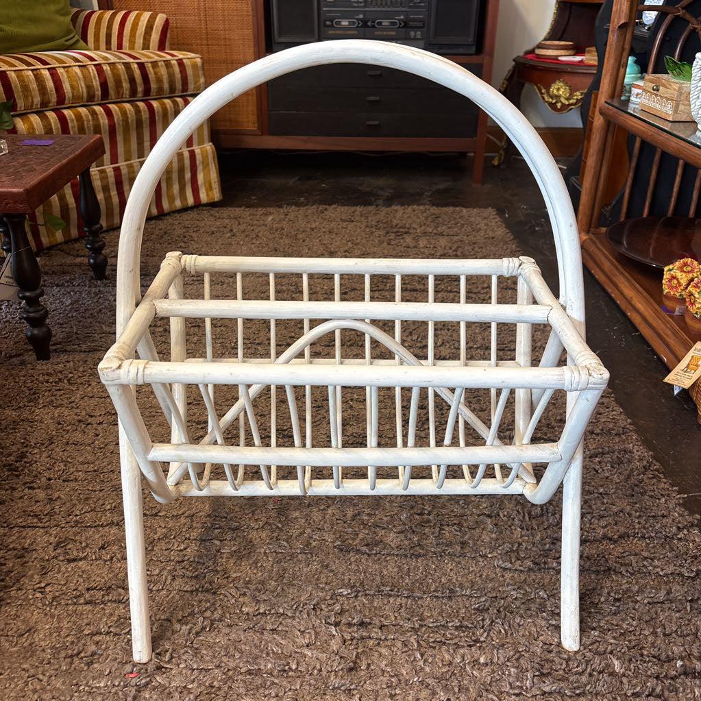 A white bamboo magazine rack with handle on a rug in a store setting.