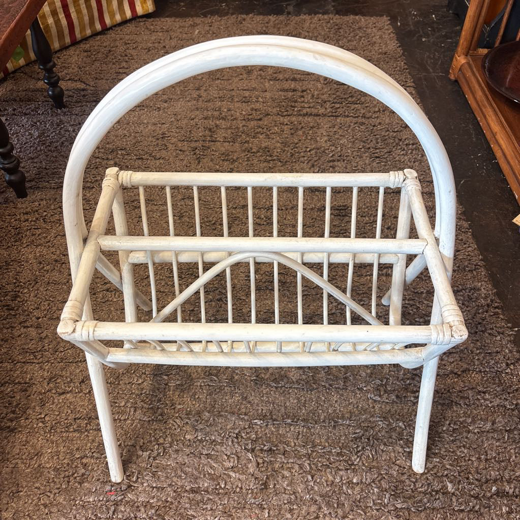A white bamboo magazine rack with handle on a rug in a store setting.
