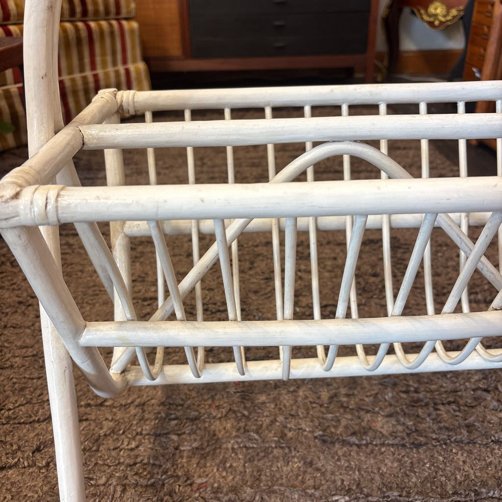A white bamboo magazine rack with handle on a rug in a store setting.