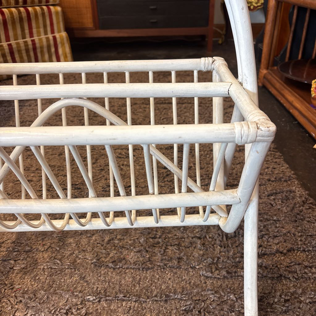 A white bamboo magazine rack with handle on a rug in a store setting.