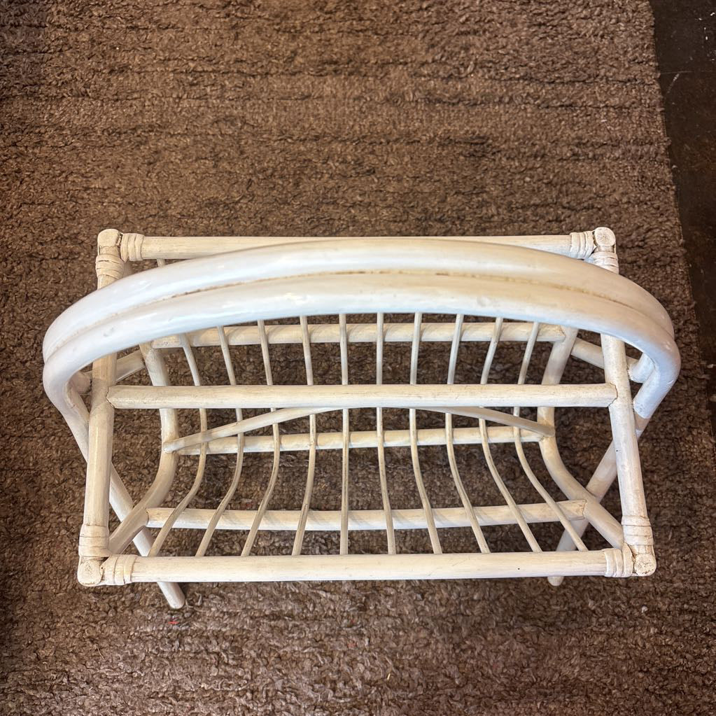 A white bamboo magazine rack with handle on a rug in a store setting.