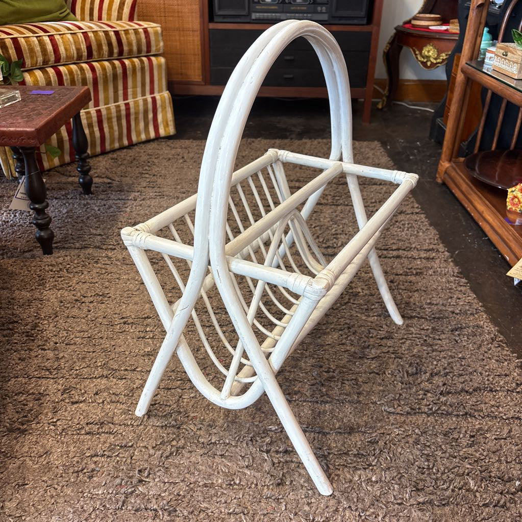 A white bamboo magazine rack with handle on a rug in a store setting.