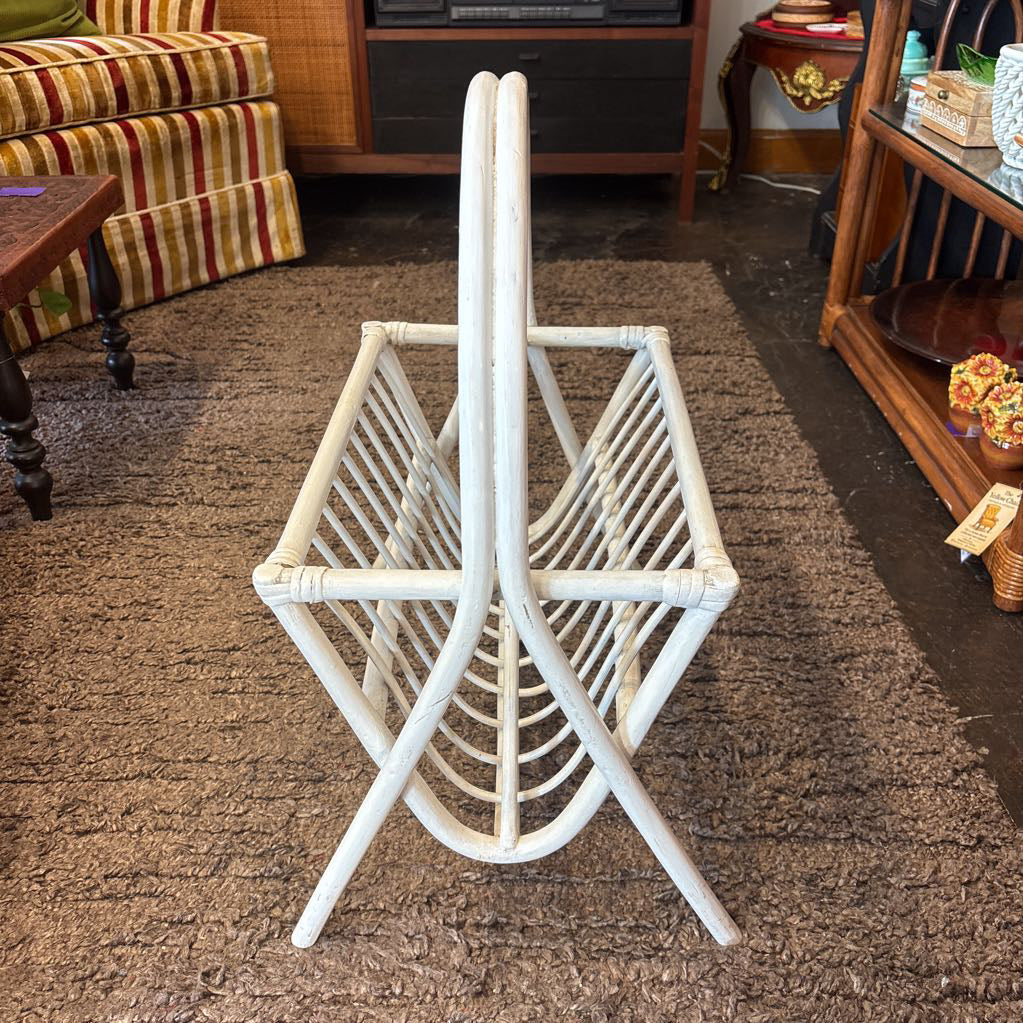 A white bamboo magazine rack with handle on a rug in a store setting.