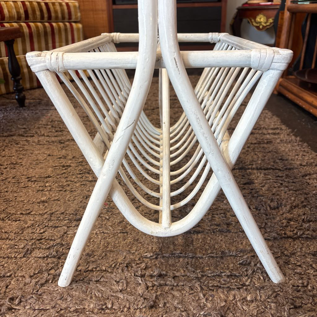A white bamboo magazine rack with handle on a rug in a store setting.