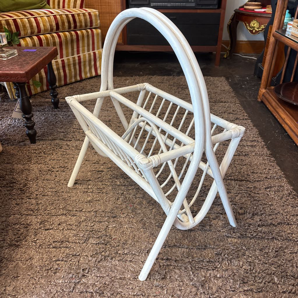 A white bamboo magazine rack with handle on a rug in a store setting.