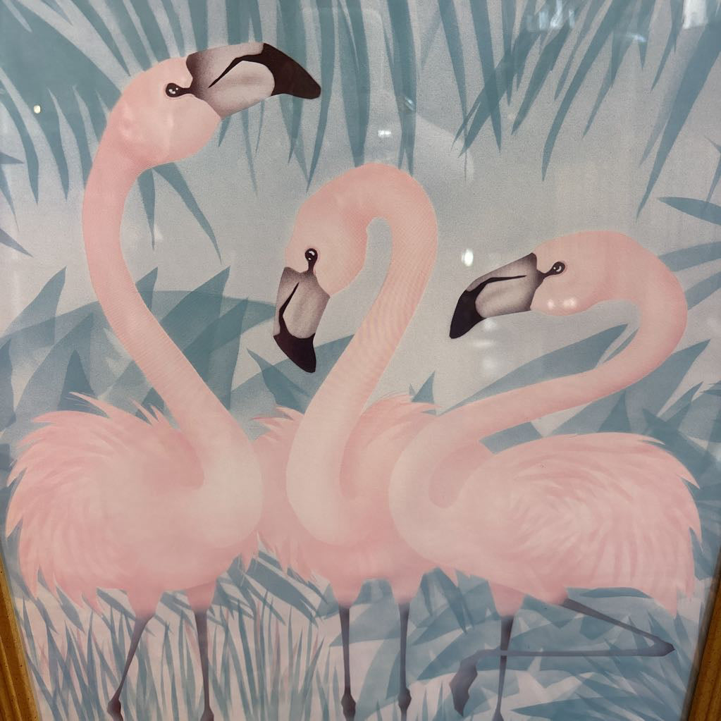 A print of three pink flamingos in a tropical setting in a gold frame in a room setting.