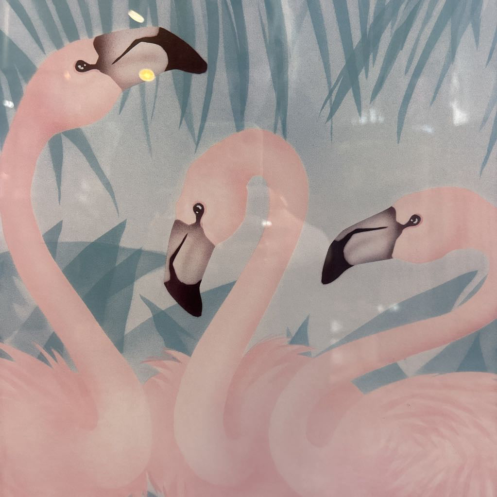 A print of three pink flamingos in a tropical setting in a gold frame in a room setting.