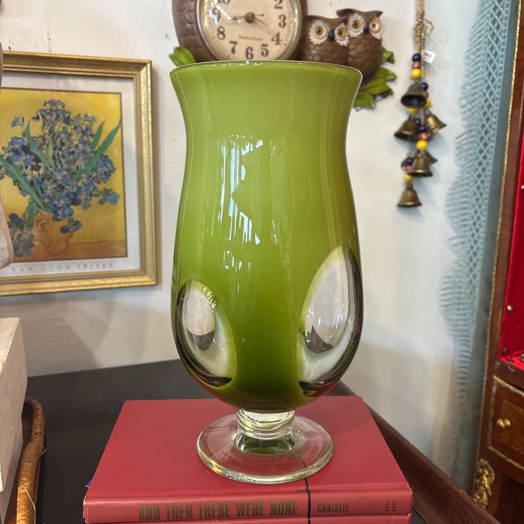 A large green glass footed vase with circular clear glass parts near the base.
