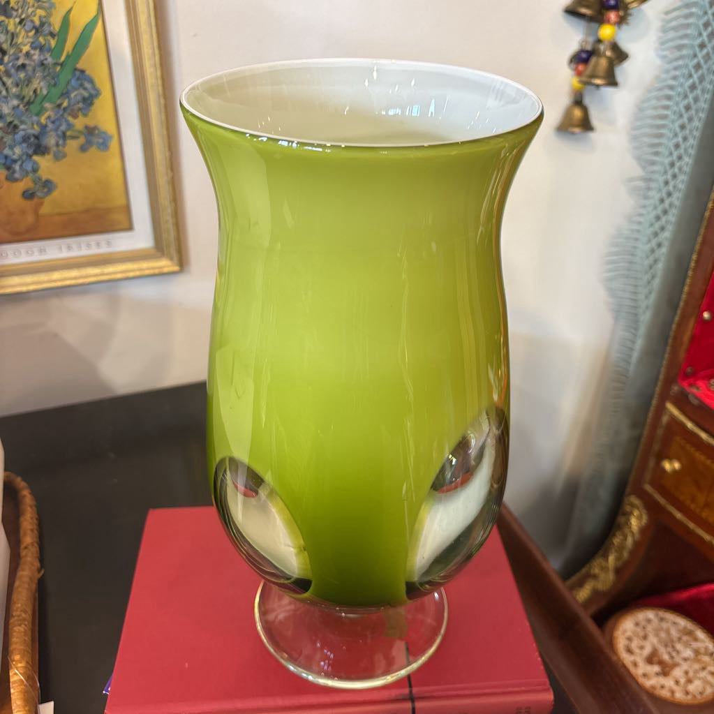 A large green glass footed vase with circular clear glass parts near the base.
