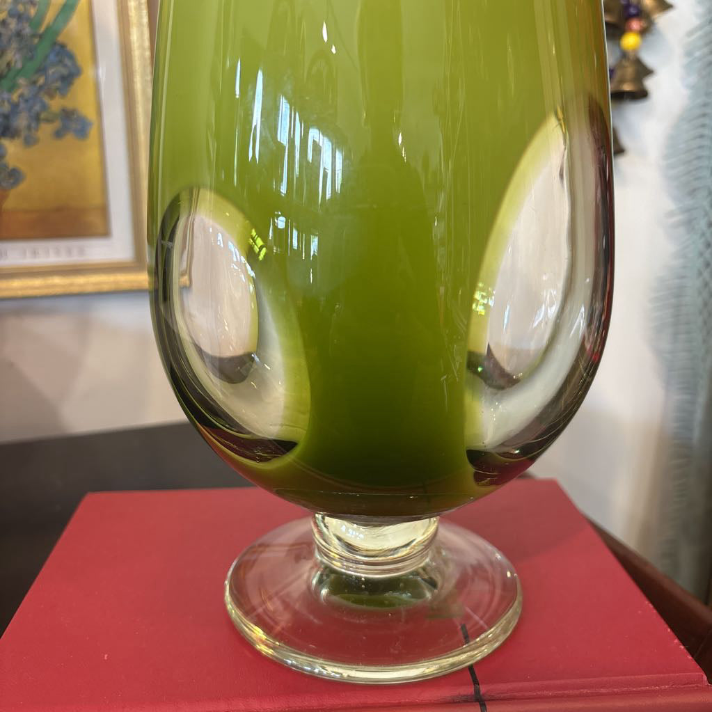 A large green glass footed vase with circular clear glass parts near the base.