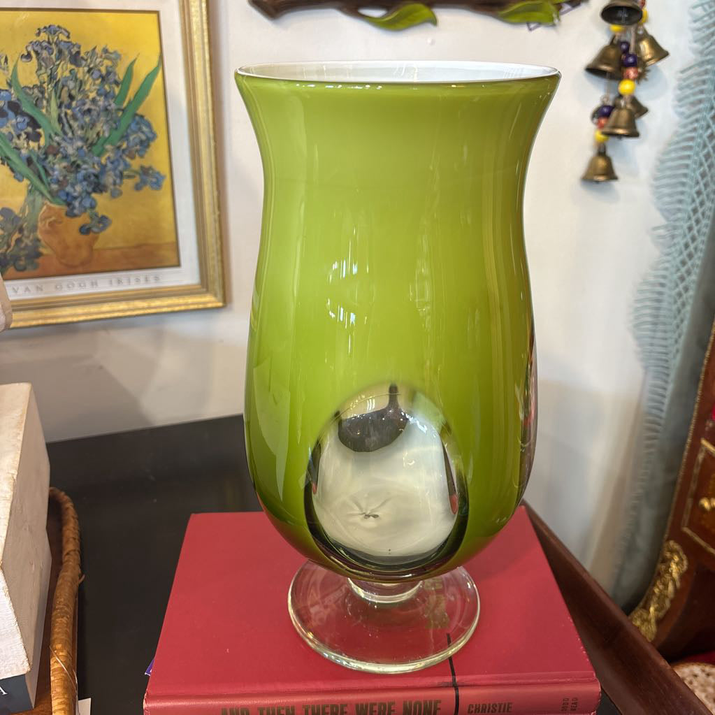 A large green glass footed vase with circular clear glass parts near the base.