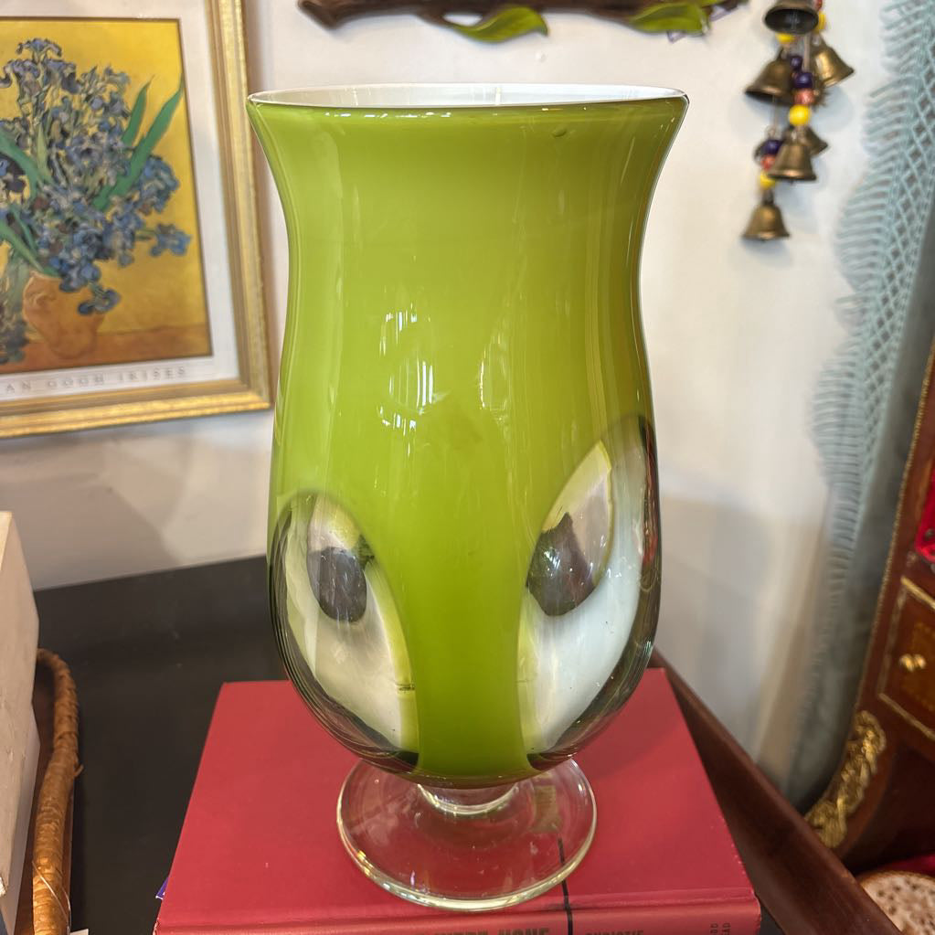 A large green glass footed vase with circular clear glass parts near the base.