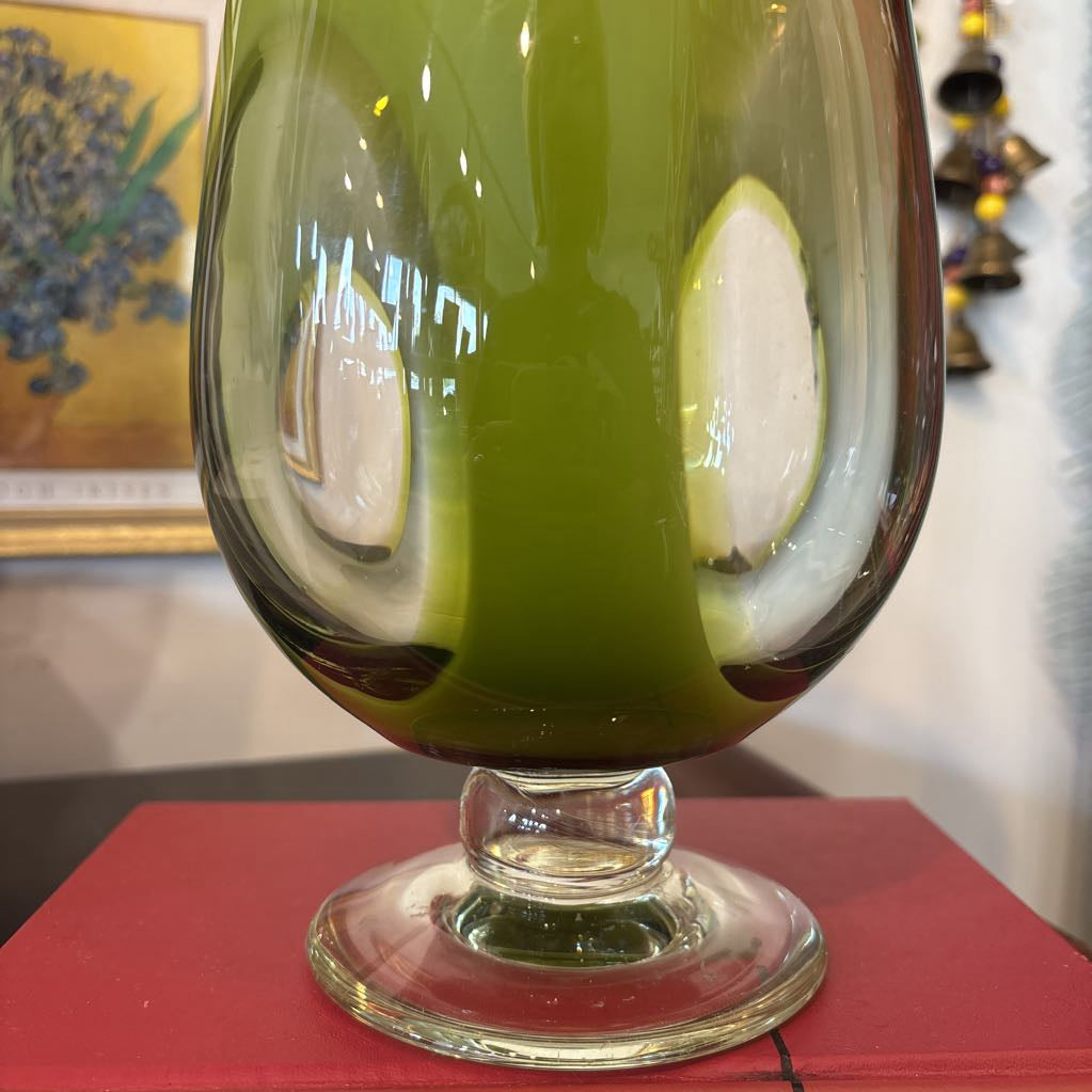 A large green glass footed vase with circular clear glass parts near the base.
