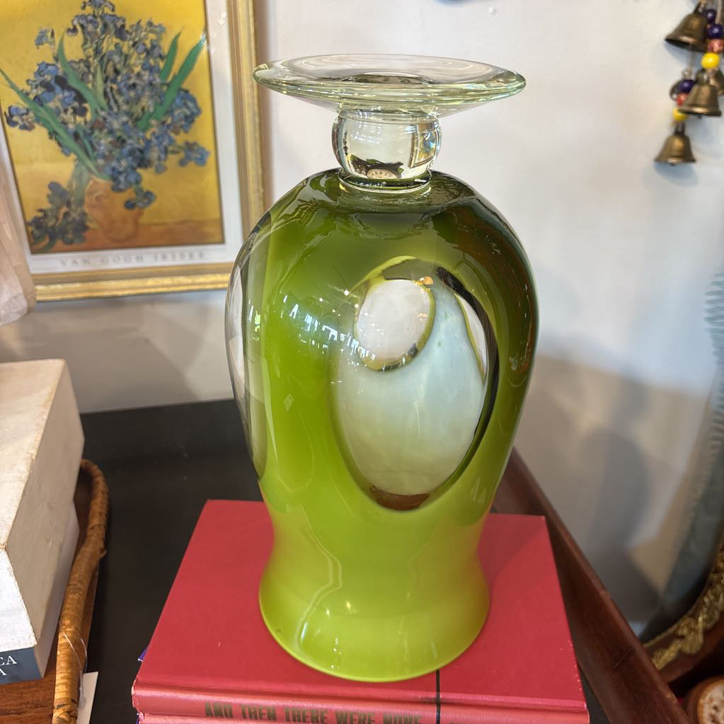 A large green glass footed vase with circular clear glass parts near the base.