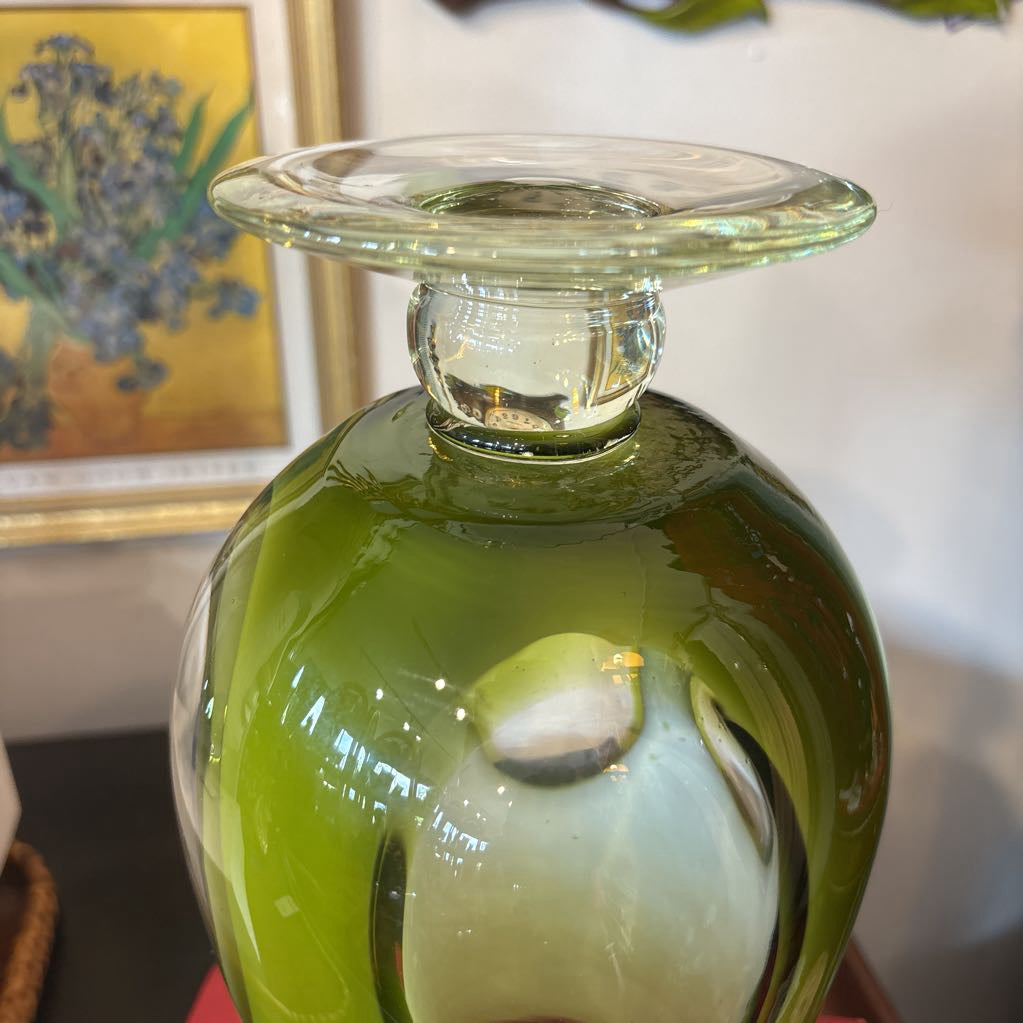 A large green glass footed vase with circular clear glass parts near the base.