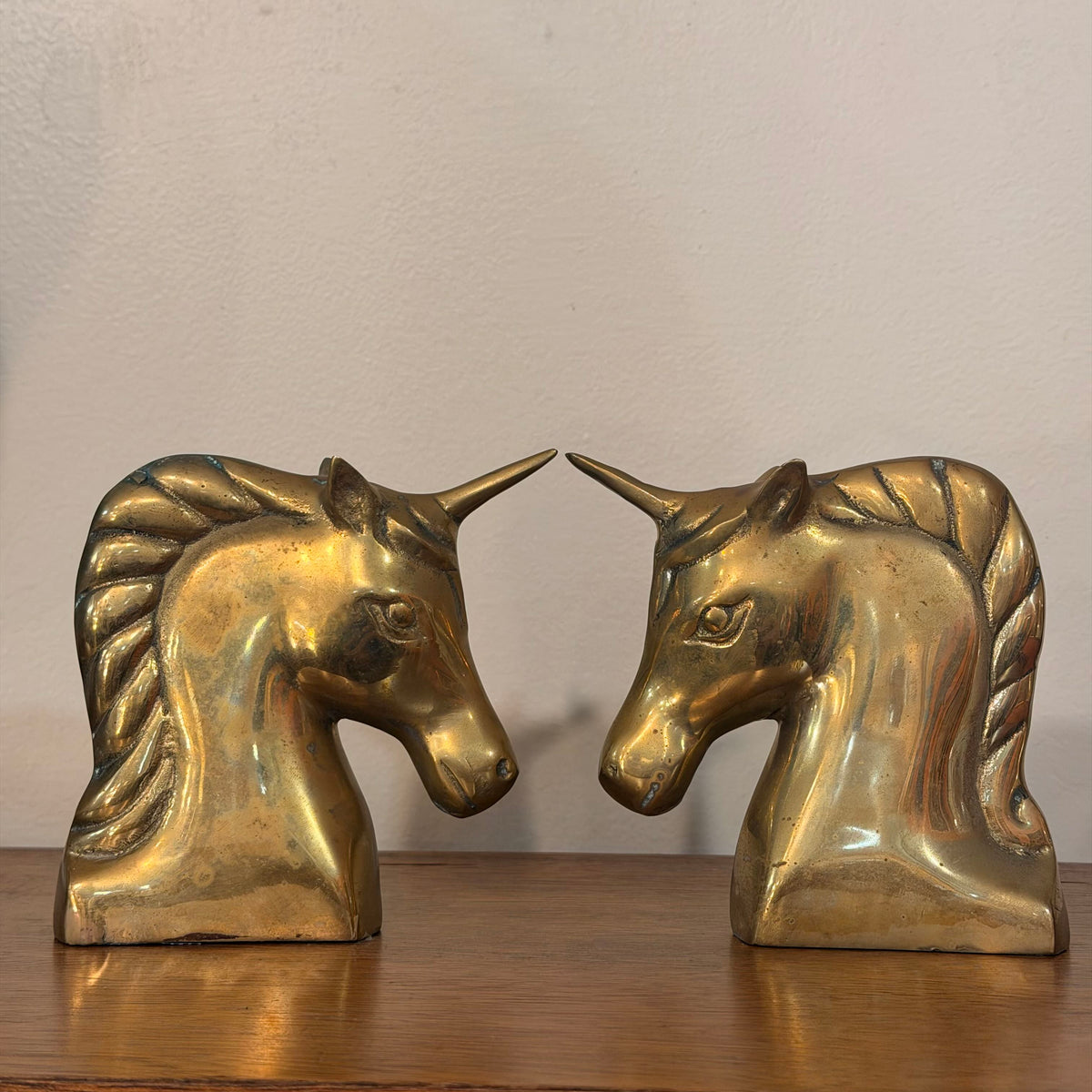 A pair of vintage brass unicorn bookends sitting on a wooden table against a plain off-white wall.